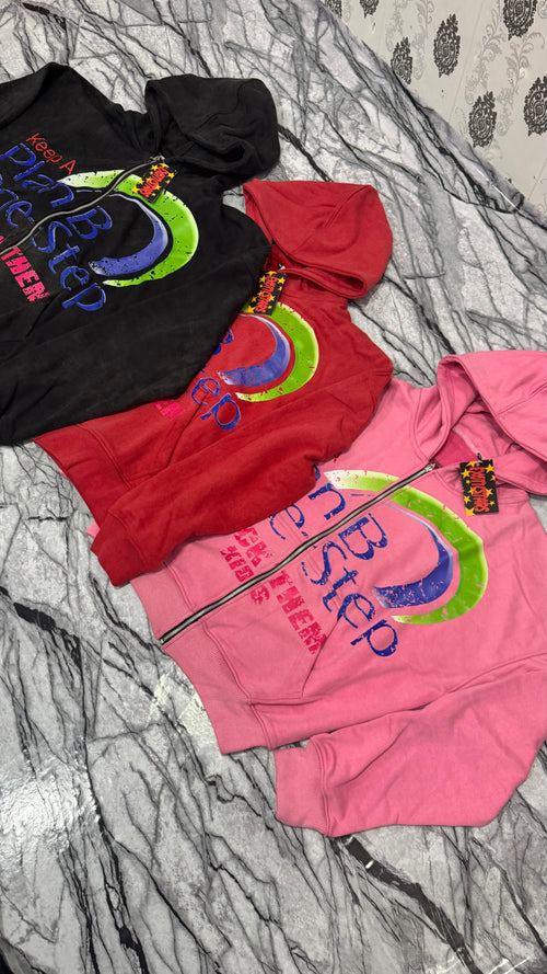 Three hoodies in black, red, and pink with colorful graphics on a textured surface.